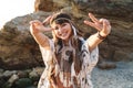 Image of hippy girl wearing feather headband showing peace sign by seaside