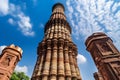 Image of the historic Qutub Minar in Delhi, India, with the towering minaret, intricate carvings, and blue sky.