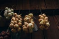 Image - illuminated bundles of onions green, red and garlic hanging against the wooden wall. Onions drying up for storage in