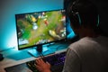 Image of immersed teenage gamer boy playing video games on computer in dark room, wearing headphones and using backlit colorful k