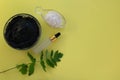 Image of the ingredients of home cosmetics. Black mask, black dirt, pink salt, a bottle with an eyedropper on a yellow background.