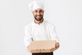 Image of joyful baker man in cook uniform smiling and holding pizza box Royalty Free Stock Photo