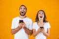 Image of joyful couple man and woman smiling while both using mobile phones, isolated over yellow background Royalty Free Stock Photo