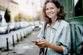 Image of joyful curly happy woman smiling and using mobile phone while walking at city street Royalty Free Stock Photo