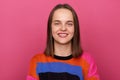 Image of joyful woman wearing sweater posing against pink wall, looking at camera with toothy smile, being in good mood, Royalty Free Stock Photo