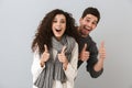 Image of joyous couple man and woman laughing and showing thumbs up at camera, isolated over gray background