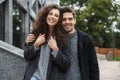 Image of joyous couple man and woman 20s in warm clothes, standing over gray building outdoor Royalty Free Stock Photo