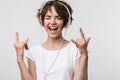 Image of joyous woman in basic t-shirt showing rock sign while listening to music with headphones Royalty Free Stock Photo