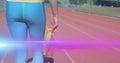 Image of light moving over midsection of woman holding running shoes walking on running track