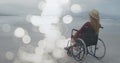 Image of light spots over disabled cuacasian woman sitting in wheelchair at beach Royalty Free Stock Photo