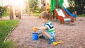 Image of little boy sitting on the playground and puring sand with small plastic spade in colorful bucket. Kid digging Royalty Free Stock Photo