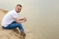 The image lonely positive and smiling man sitting on a beach by the river. Royalty Free Stock Photo
