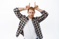 Image of man with red hair looking sassy and confident, showing bull horns gesture and staring macho at camera, standing