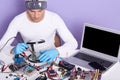 Image of man using magnifier while looking on wires of pc, concentrated male working in electronic lab, sits at table surrounded
