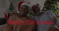 Image of merry christmas text over senior african american couple wearing santa hats Royalty Free Stock Photo