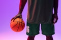 Image of midsection of african american basketball player with basketball on neon purple background