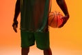 Image of midsection of african american basketball player with basketball on neon orange background