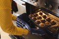 Image of midsection of african american senior woman taking out cupcakes from oven