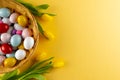 Image of multi coloured easter eggs in basket with yellow tulips and copy space on yellow background Royalty Free Stock Photo