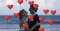 Image of multiple red heart balloons floating over newly married couple embracing on beach Royalty Free Stock Photo