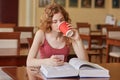 Image of pensive intelligent sweet curly haired girl, holding papercup of drink in one hand, drinking coffee, using her smartphone