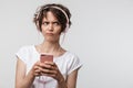 Image of perplexed woman in basic t-shirt holding smartphone while listening to music with headphones