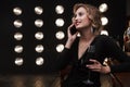 Image of pleased blonde woman using cellphone and drinking red wine in bar