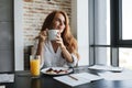 Image of pleased ginger businesswoman smiling and having breakfast