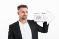 Image of pleased man wearing black jacket looking on speech arrow pointer with word vacancy holding in hand, isolated over white