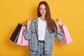 Image of portrait of happy smiling woman holding rose and black shopping bags. Female model isolated over yellow studio background Royalty Free Stock Photo