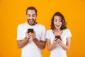 Image of positive couple man and woman smiling while both using mobile phones, isolated over yellow background Royalty Free Stock Photo