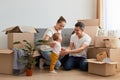 Image of positive family having rest while unpacking moving box at their new house, sitting on floor near sofa and playing with Royalty Free Stock Photo