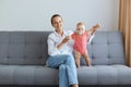 Image of positive optimistic woman wearing white shirt and jeans sitting on sofa with her tiny daughter, baby in pink bodysuit Royalty Free Stock Photo