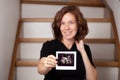 Image of pregnant smiling caucasian curly woman sitting on wooden stairs and posing while showing ultrasound scans on