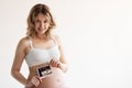 Image of pregnant smiling woman standing and posing while showing ultrasound scans over grey background Royalty Free Stock Photo