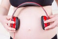 Close up of pregnant woman with headphones on the belly listening to music