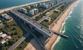 aerial view coastal city with highway overpass, beach, and ocean, with buildings and greenery along the