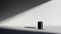 A black cylindrical object with a lid sits on a circular base, casting a shadow on a white wall. Royalty Free Stock Photo