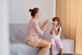 Image of professional female speech pathologist having lesson with little girl, people sitting on comfortable sofa near window,