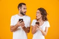 Image of puzzled couple man and woman using smartphones together, isolated over yellow background