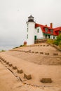 Quaint lighthouse attached to a red roofed farmhouse stands on top of a sloping tan shoreline