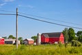 Red barn and green fields with tractors and a telephone pole with wires cutting through blue sky Royalty Free Stock Photo