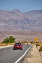 Red car driving down desert road leading to sharp turn and mountains Royalty Free Stock Photo