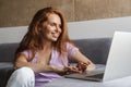 Image of redhead woman smiling and using laptop while sitting on floor Royalty Free Stock Photo