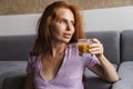 Image of redhead pleased woman drinking juice while sitting on floor Royalty Free Stock Photo