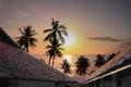 Image of resort roofs with silhouette palm trees, beach and bright sunset reflection on ocean waves and peaceful colorful twilight Royalty Free Stock Photo