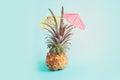 Image with ripe pineapple with parasol over blue background. Summer holidays and tropical theme Royalty Free Stock Photo