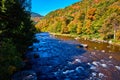 River with small rapids in shade along sunny hills of fall foliage Royalty Free Stock Photo