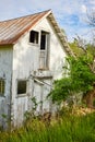 Run down abandoned white building in country with gnarly tree and busted door and window