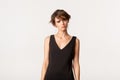 Image of sad timid girl in black dress feeling offended, looking upset over white background